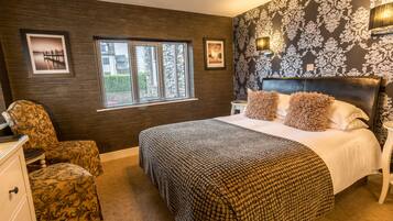 A bedroom with a large bed, a chair, a dresser, a window, and a wall with a floral pattern.
