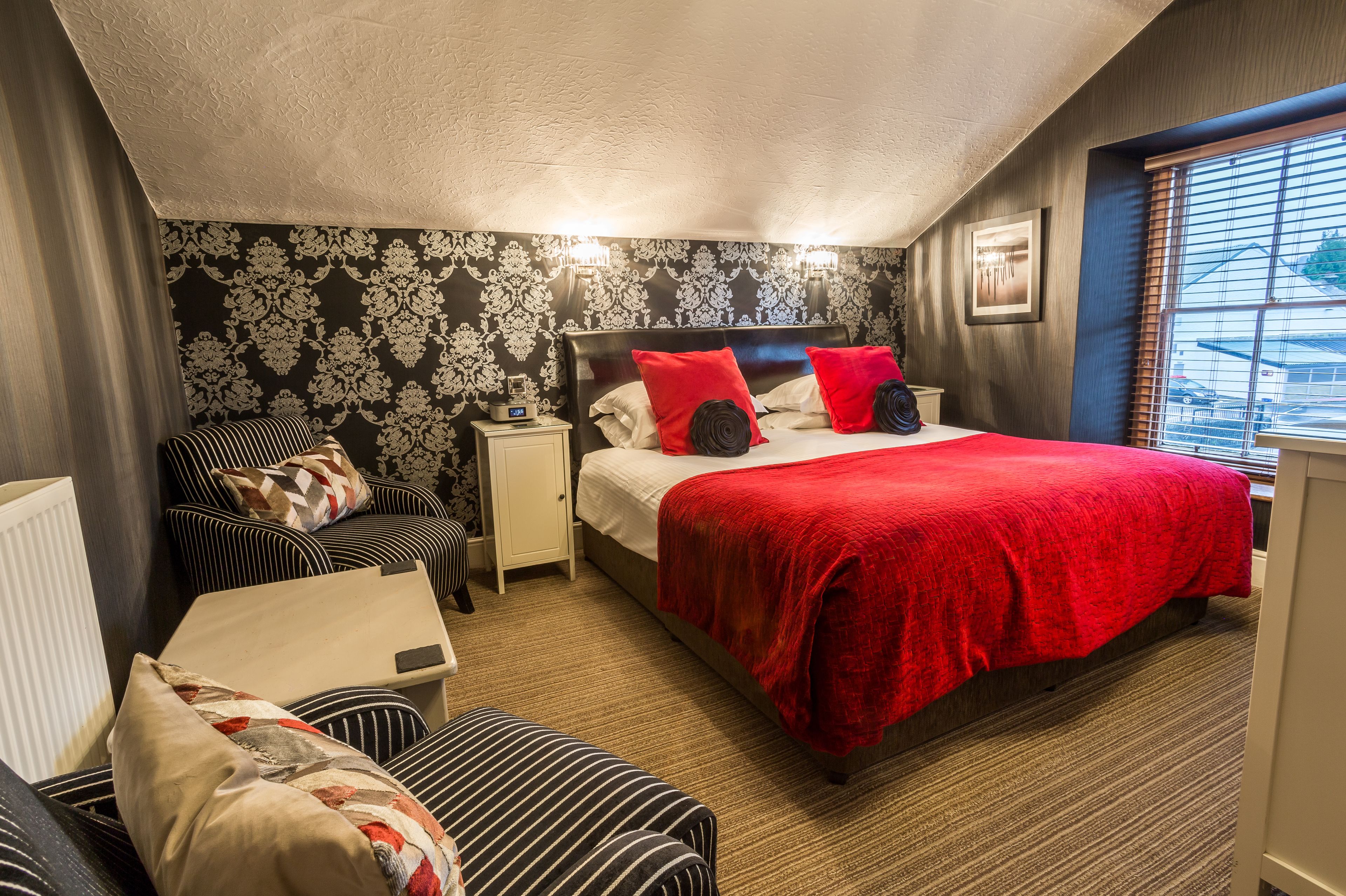 A hotel room with a bed, a chair, a nightstand, and a window with blinds.