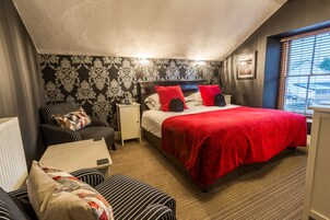 Une chambre d’hôtel avec un lit, une chaise, une table de chevet et une fenêtre avec des stores.