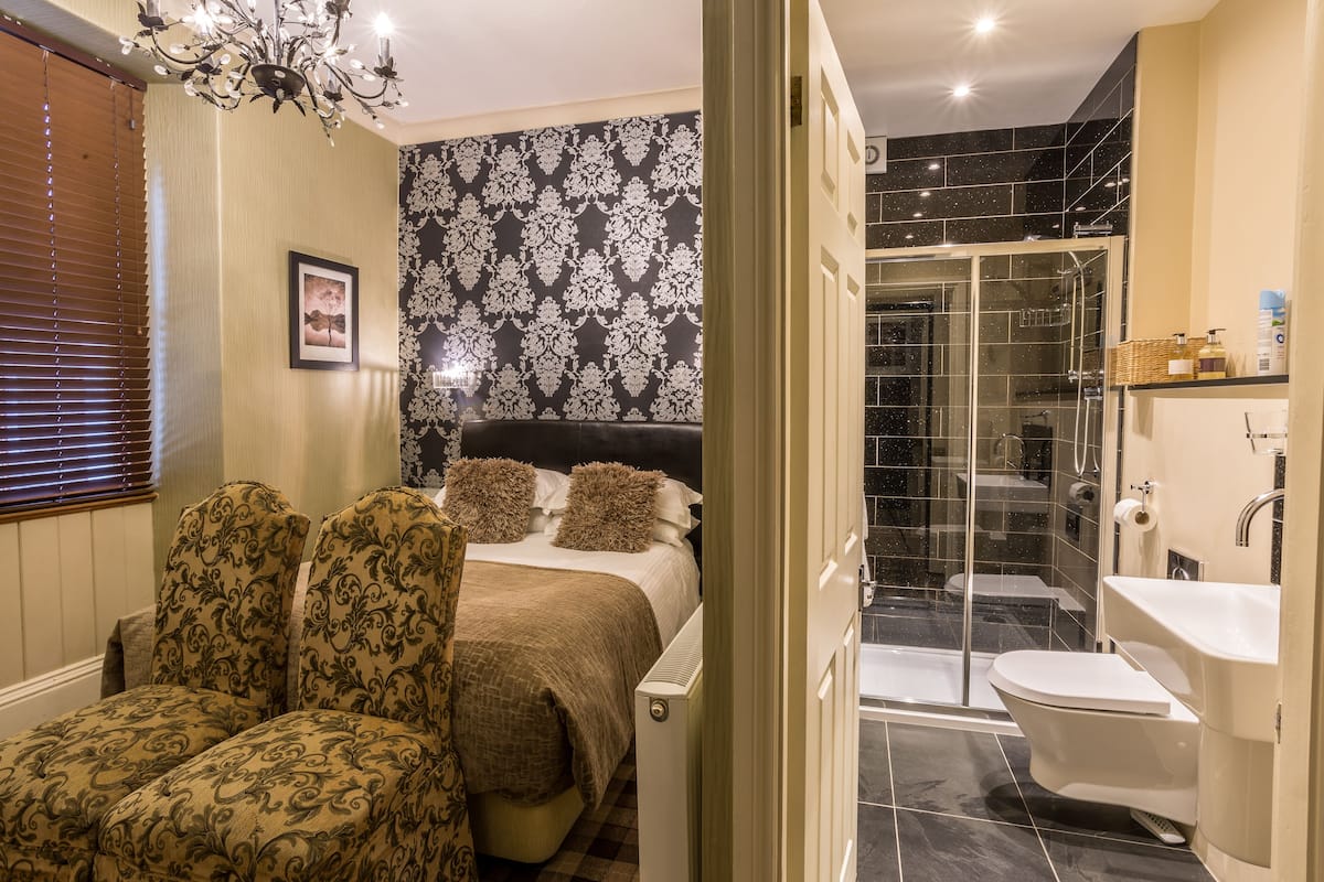 A bedroom with a bed, two upholstered chairs, a bedside table, and a chandelier.