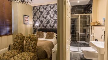 A bedroom with a bed, two upholstered chairs, a bedside table, and a chandelier.