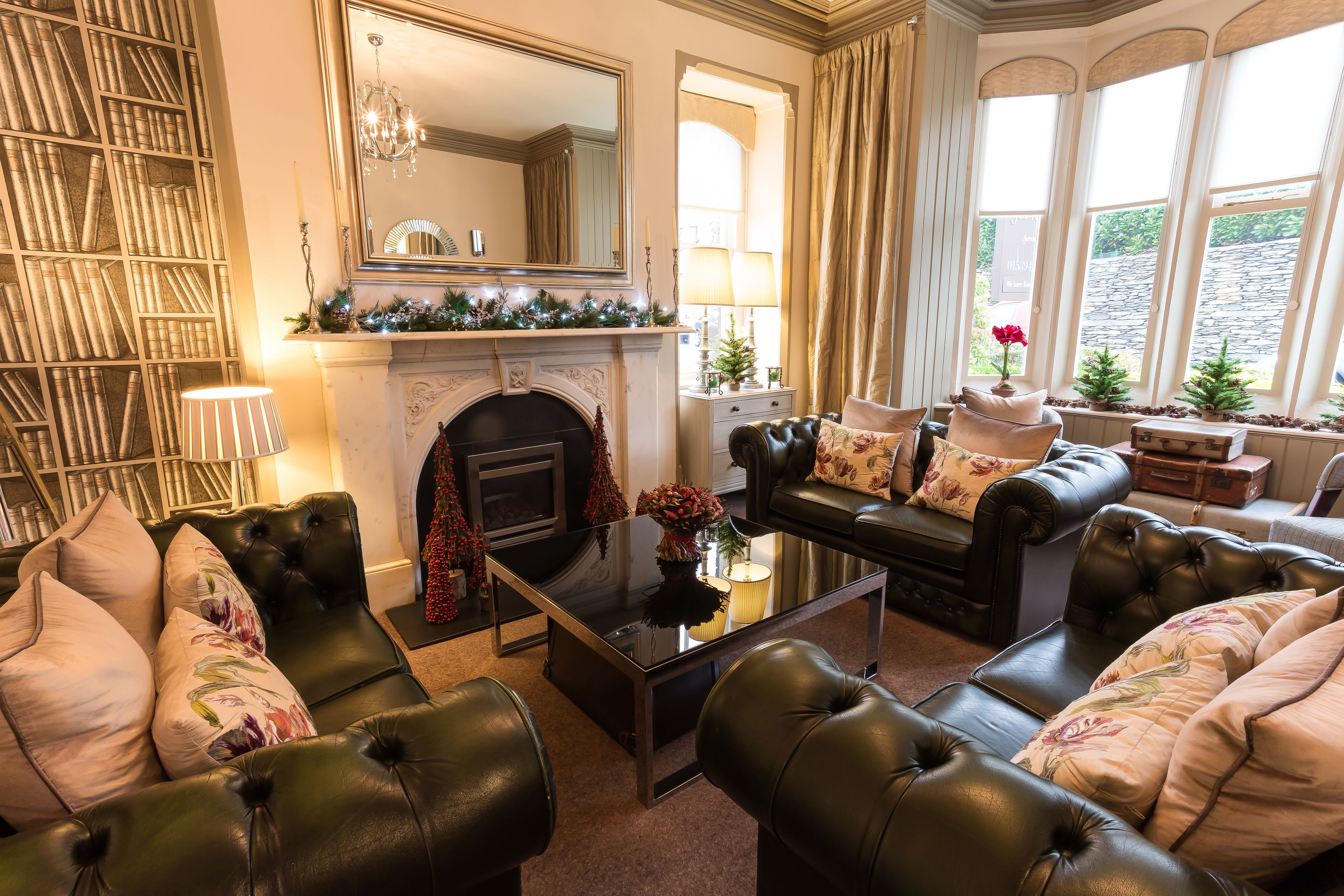 A cozy living room with leather sofas, a fireplace, a bookshelf, and large windows.