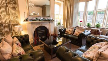 A cozy living room with leather sofas, a fireplace, a bookshelf, and large windows.
