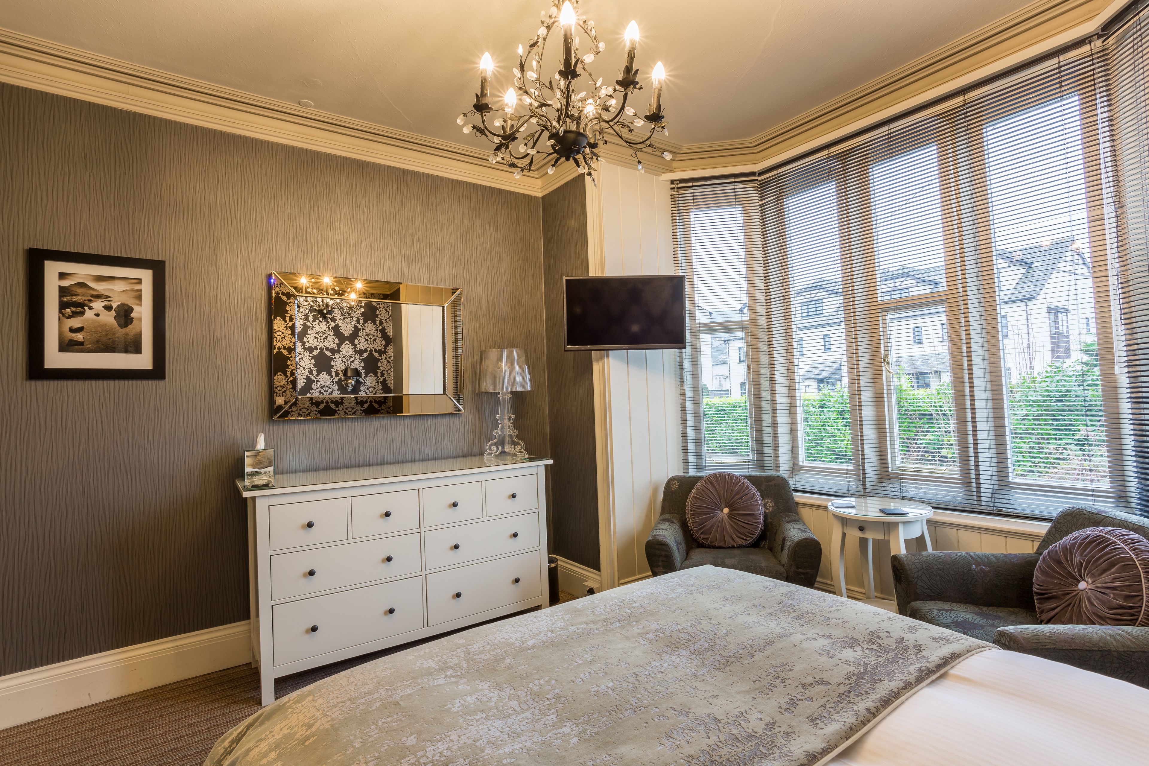 A bedroom with a large bed, a dresser, a TV, and a window with blinds.