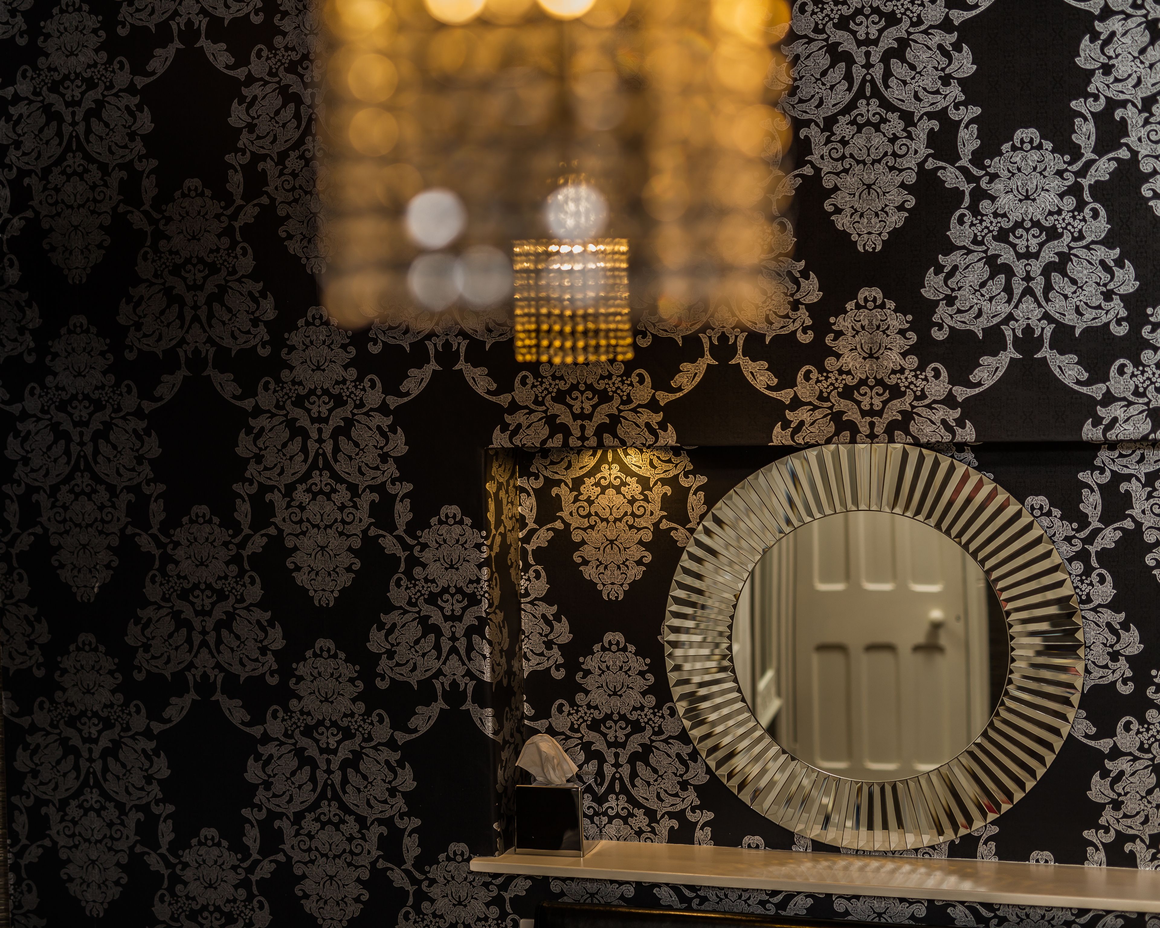 A bathroom with ornate wallpaper, a mirror, and a tissue box.