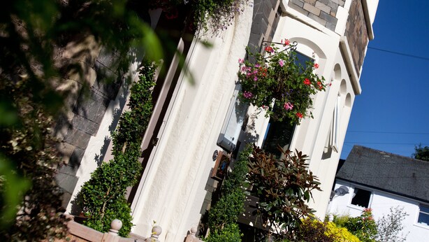 Un edificio con fachada blanca, una escalera de piedra y macetas colgantes de flores.