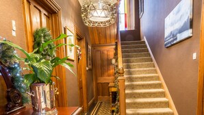 Un hall de hotel con un mostrador de recepción de madera, una planta en maceta, una escalera con alfombra estampada y un candelabro.