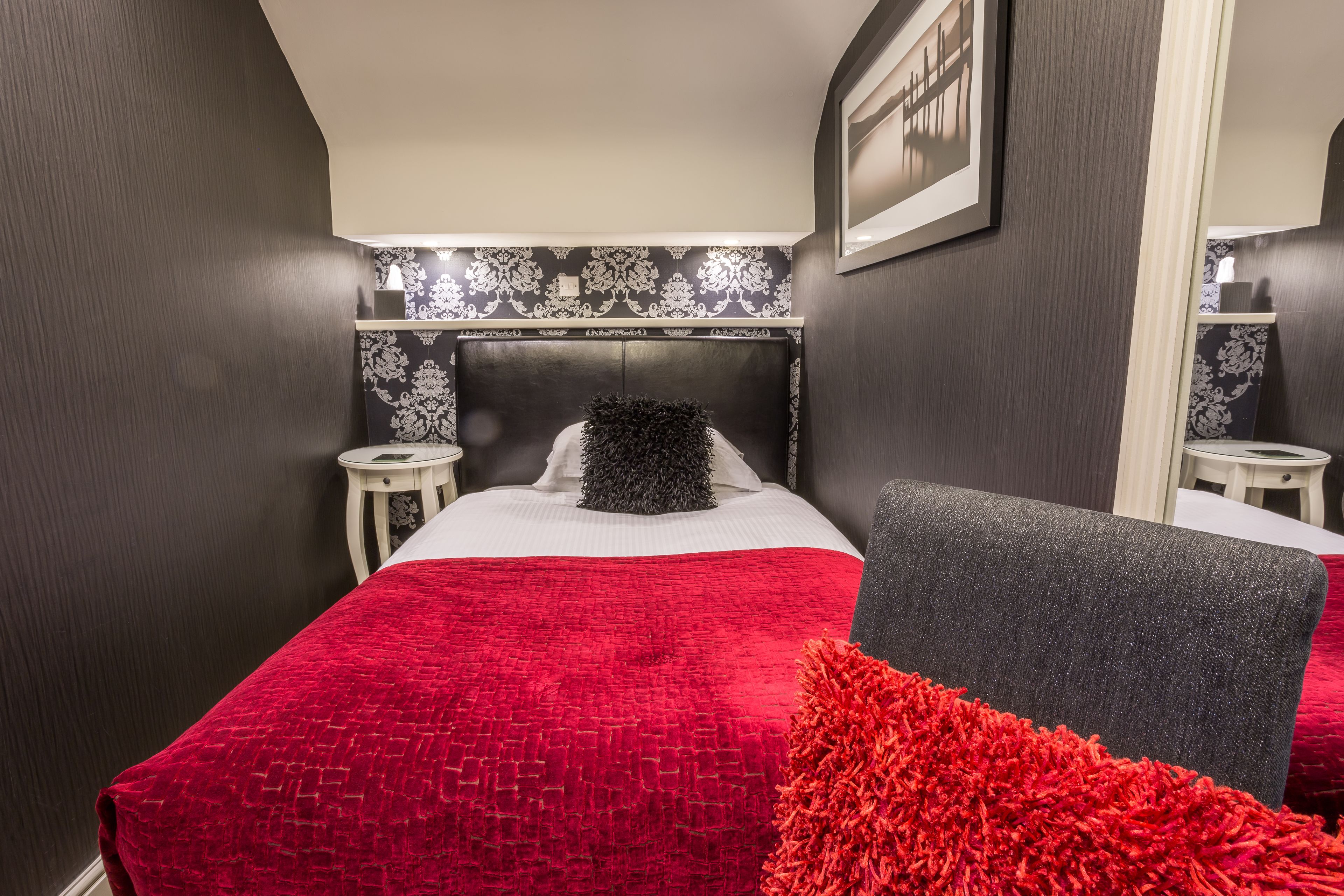 A bedroom with a large bed, a headboard, a nightstand, a chair, and a mirror.