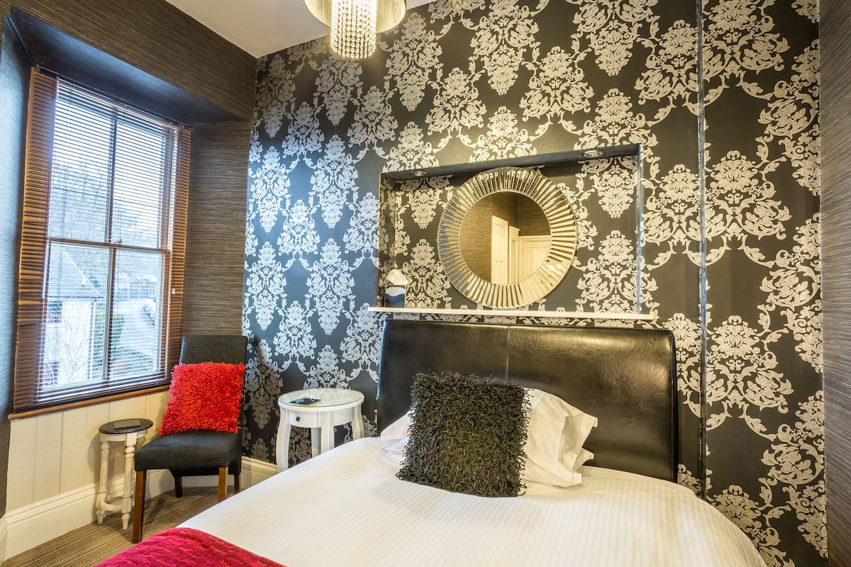 A bedroom with a large bed, a chair, a small table, and a mirror on the wall.
