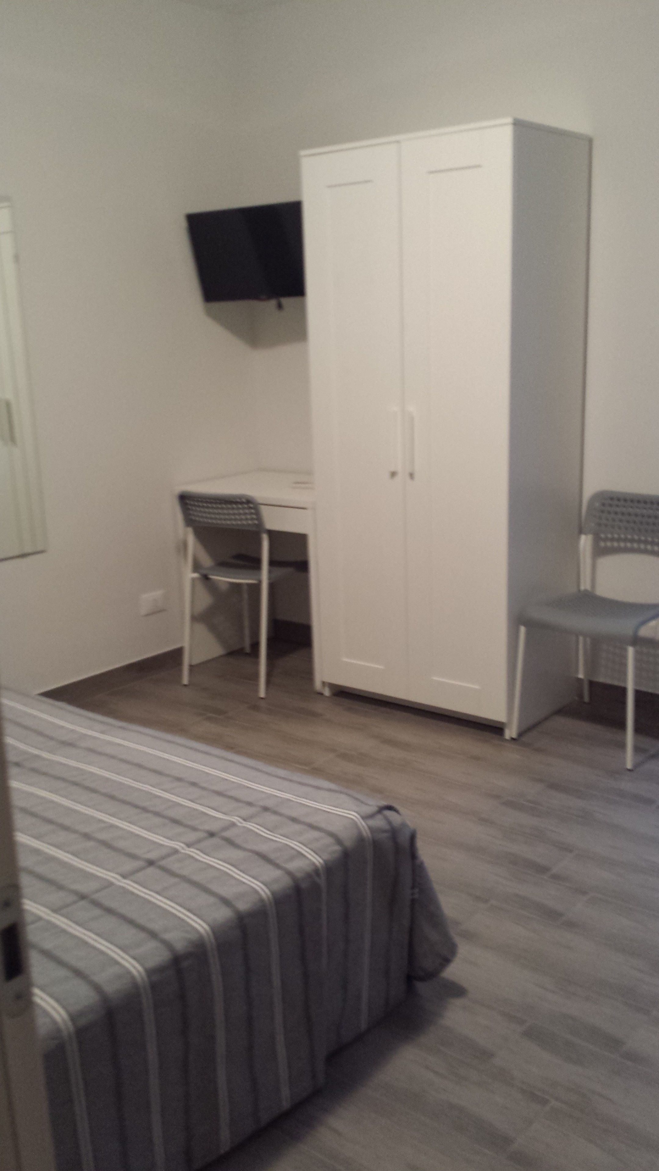 A bedroom with a bed, a desk, two chairs, and a wardrobe.