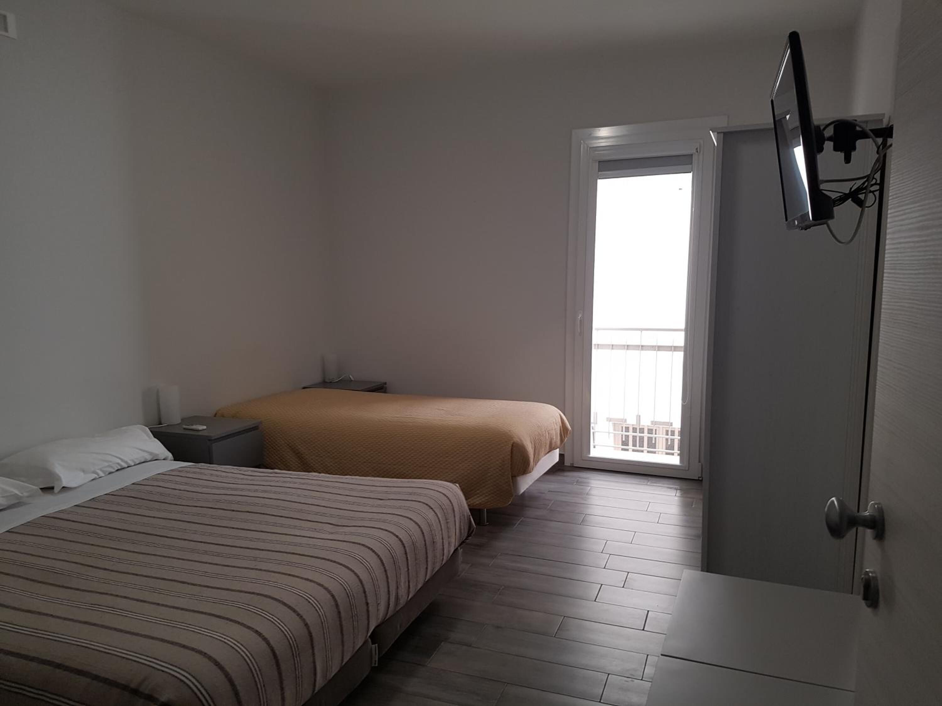 A bedroom with two beds, a TV mounted on the wall, and a door leading to a balcony.