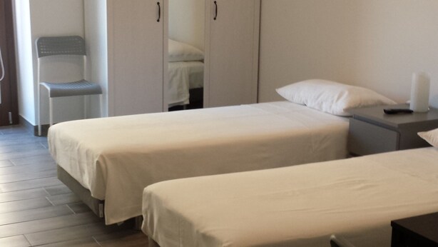 A hotel room with two single beds, a wardrobe, a chair, and a bedside table. - Beda Ragusa (Ragusa)