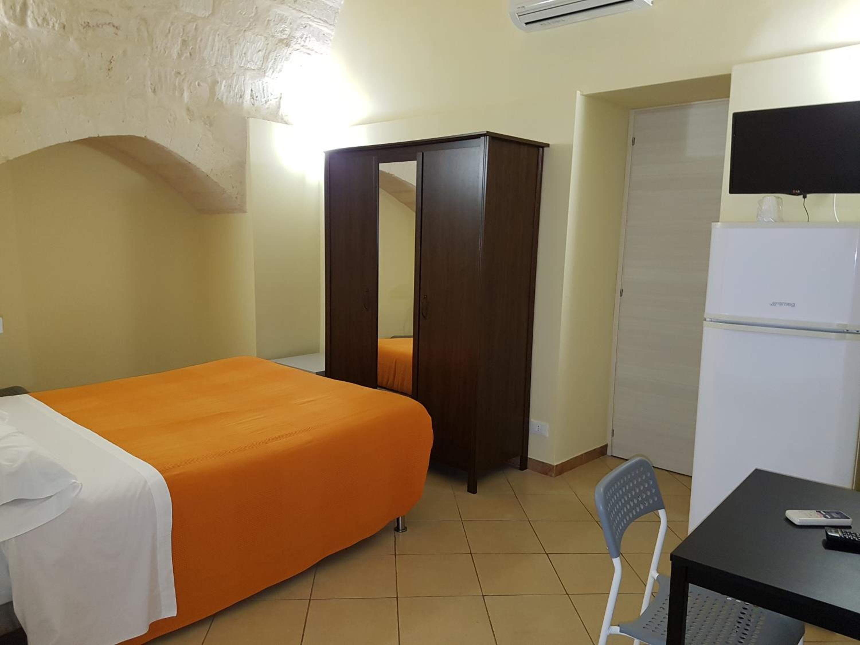 Una habitación con cama, armario, televisor y refrigerador.