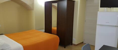 Una habitación con cama, armario, televisor y refrigerador.