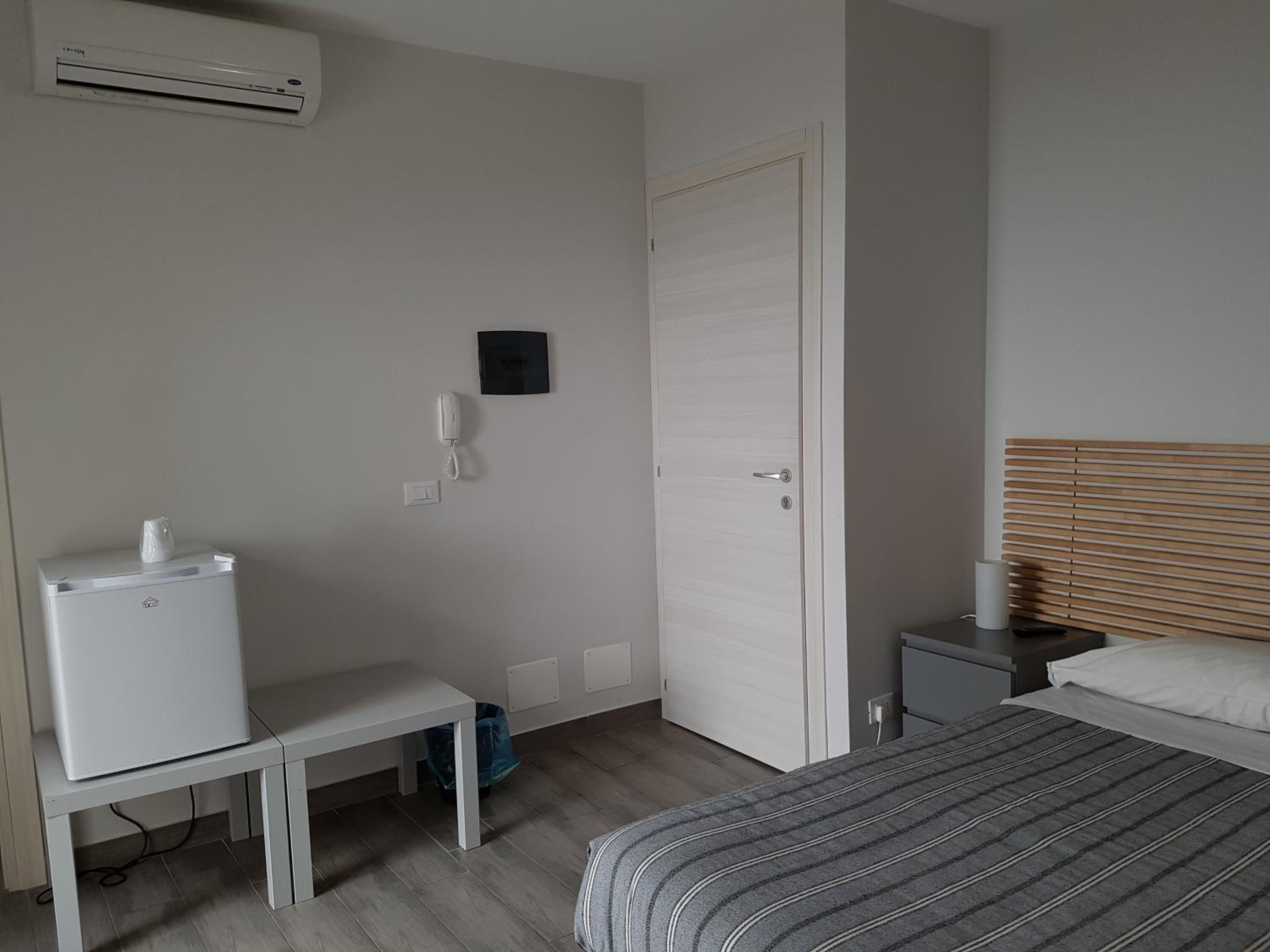Una habitación pequeña y limpia con cama, escritorio, silla, mesita, teléfono y aire acondicionado.