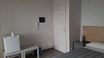 Una habitación pequeña y limpia con cama, escritorio, silla, mesita, teléfono y aire acondicionado.