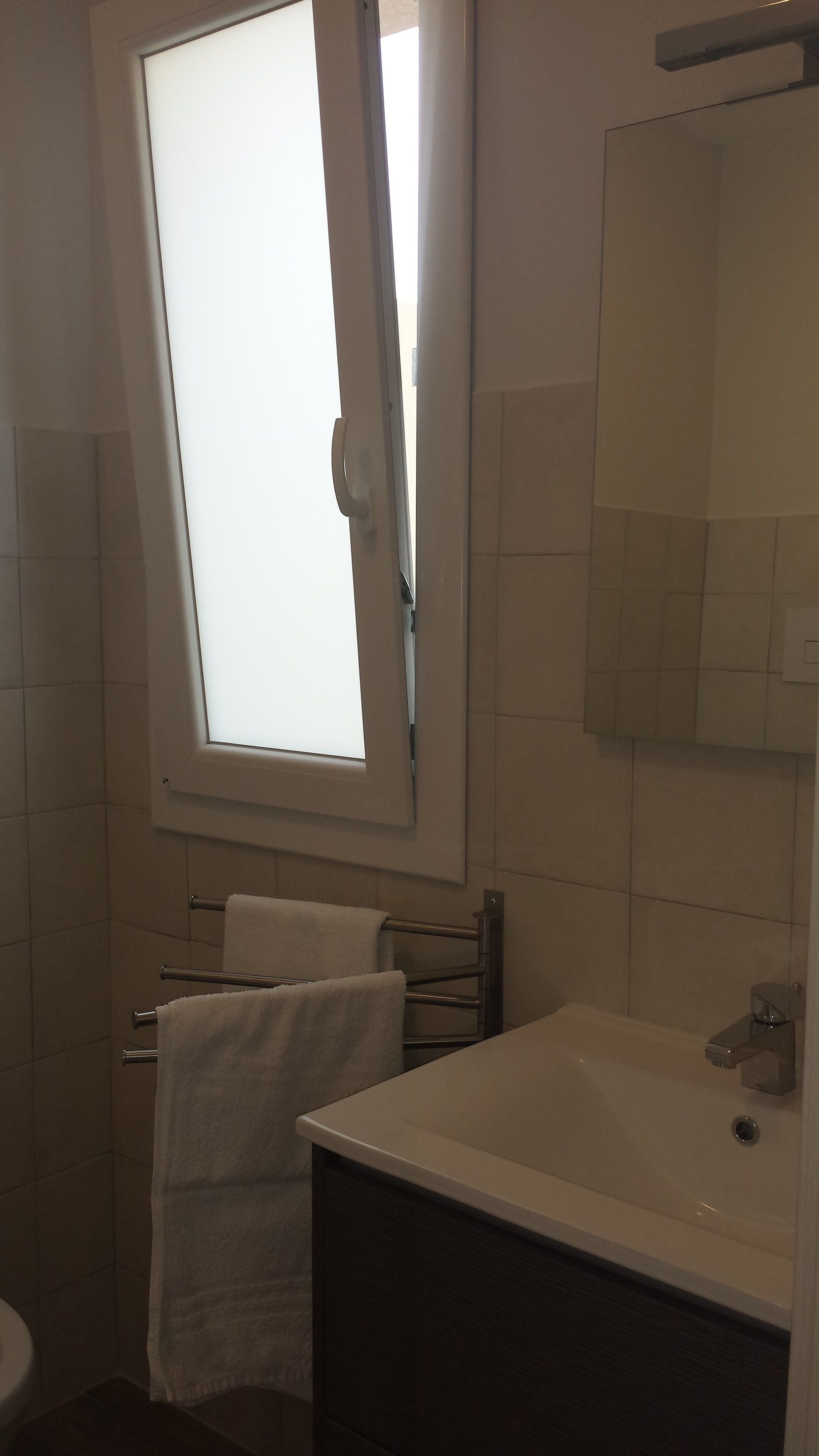 Un baño con ventana, lavabo y toallero.