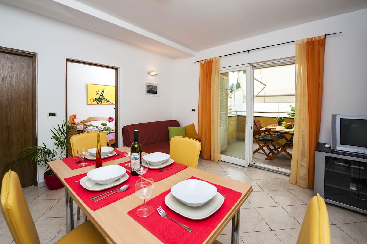 Un comedor con una mesa dispuesta para cuatro personas, un sofá y un televisor.