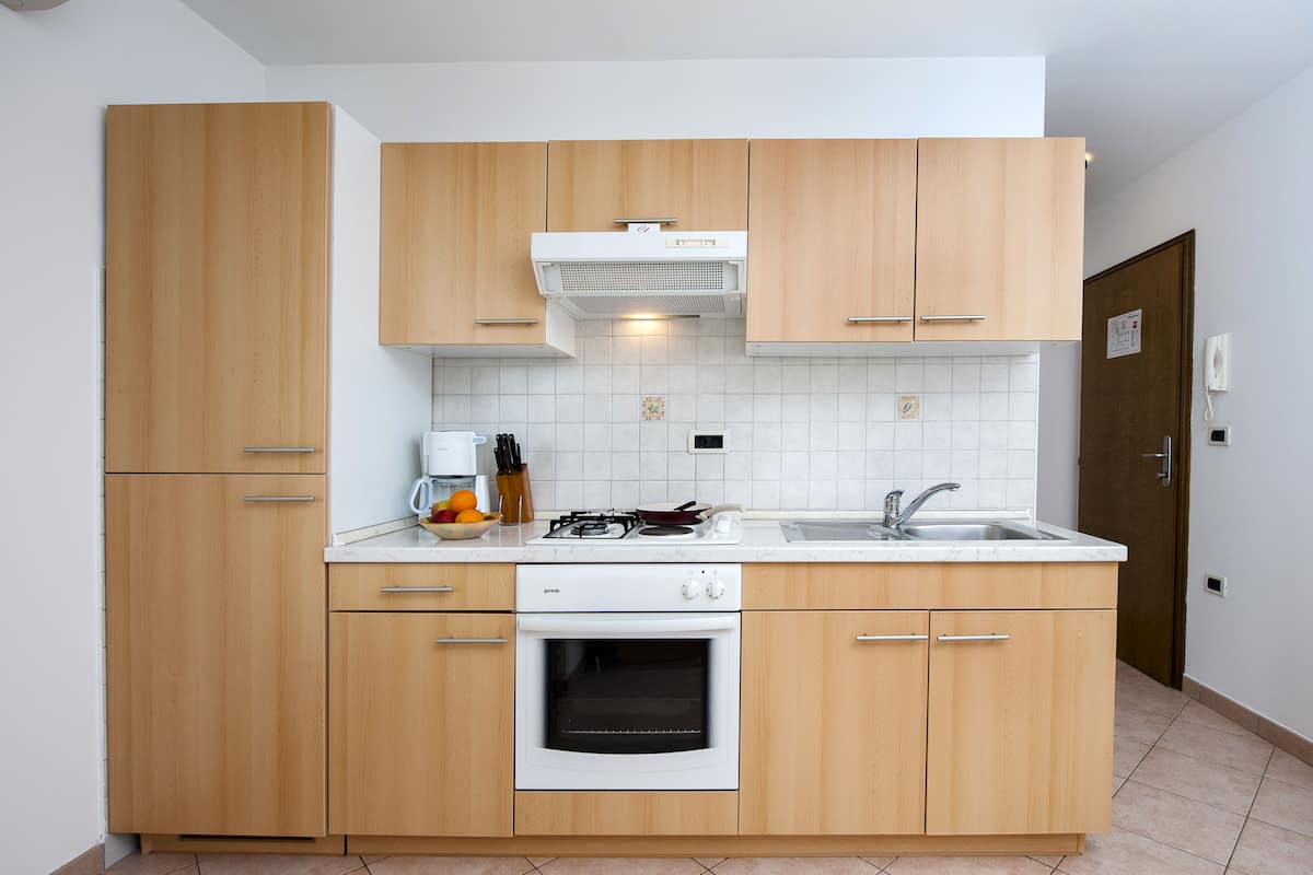 Una cocina compacta con armarios de madera, horno integrado, estufa a gas y encimera blanca.