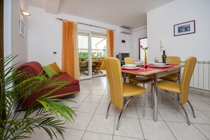 Un comedor con una mesa lista para cuatro personas, sillas amarillas, un sofá rojo y un ventanal corredero que da a un balcón.