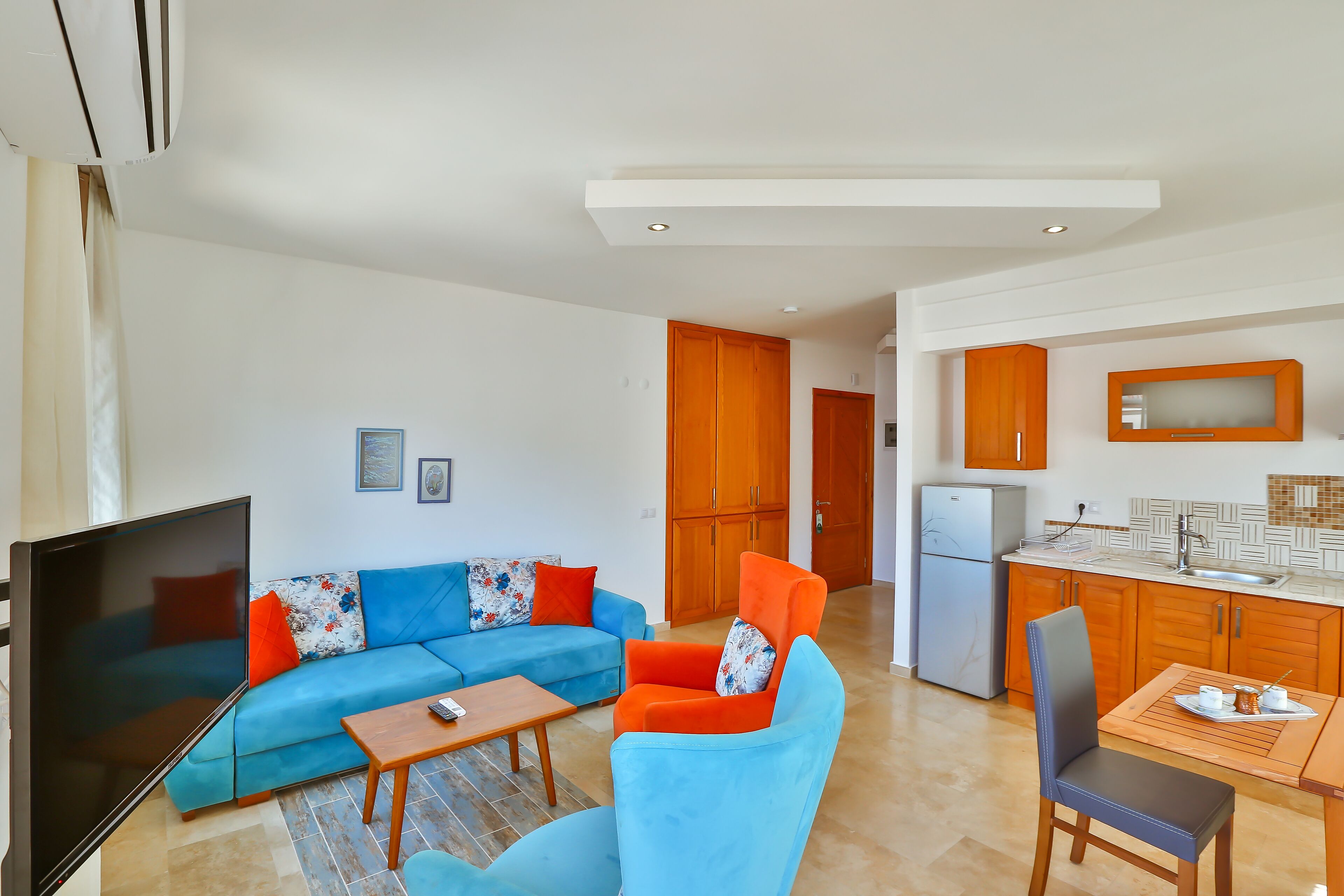 Un salon moderne comprenant un canapé d’angle, un téléviseur à écran plat, une table basse en bois et un coin repas avec une table et des chaises.