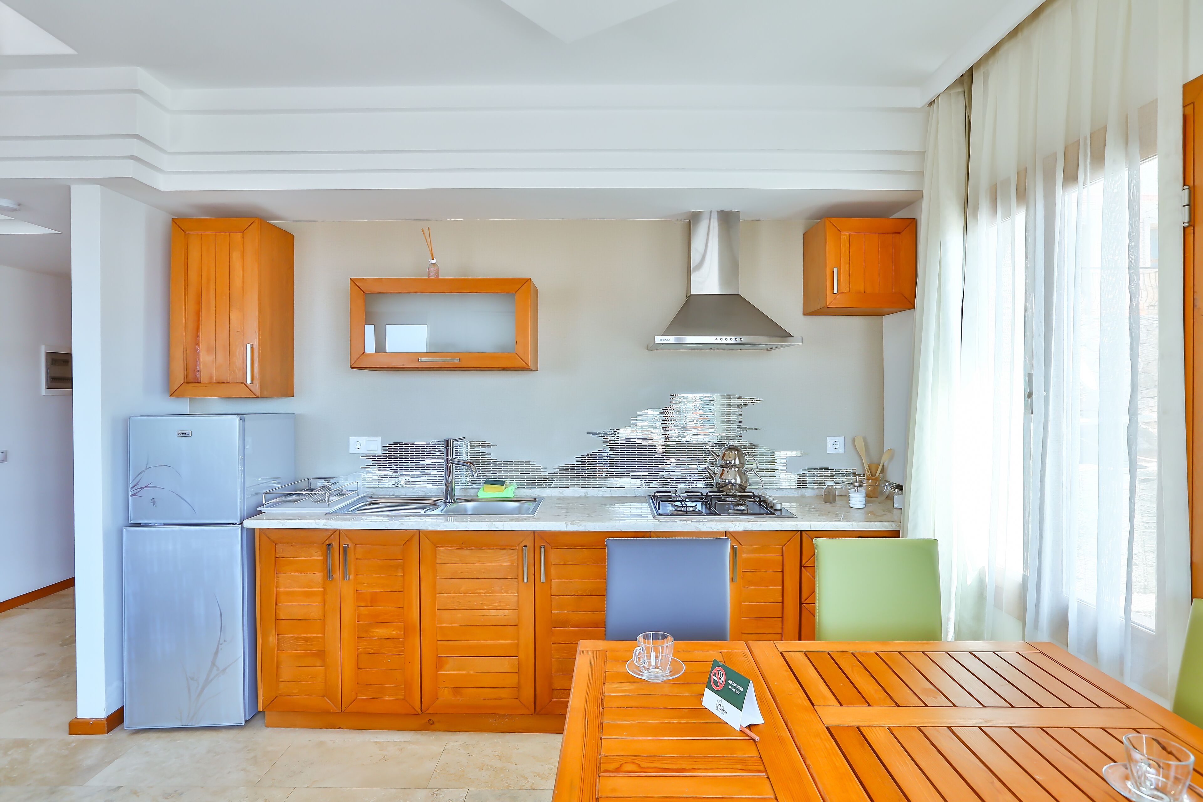 A modern kitchen with wooden cabinets, a stainless steel range hood, and a dining area with a table and chairs.