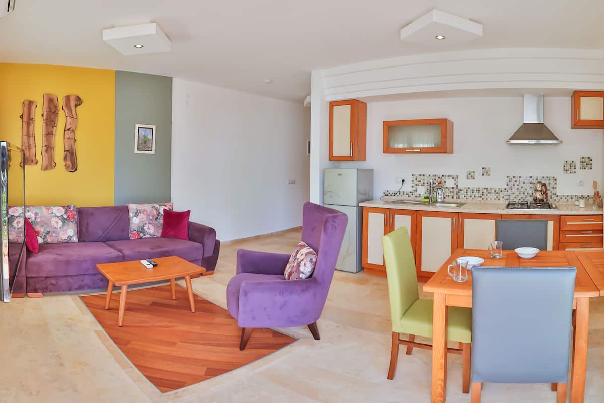 A modern living room with a purple sofa, a wooden coffee table, and a dining area with a wooden table and chairs.