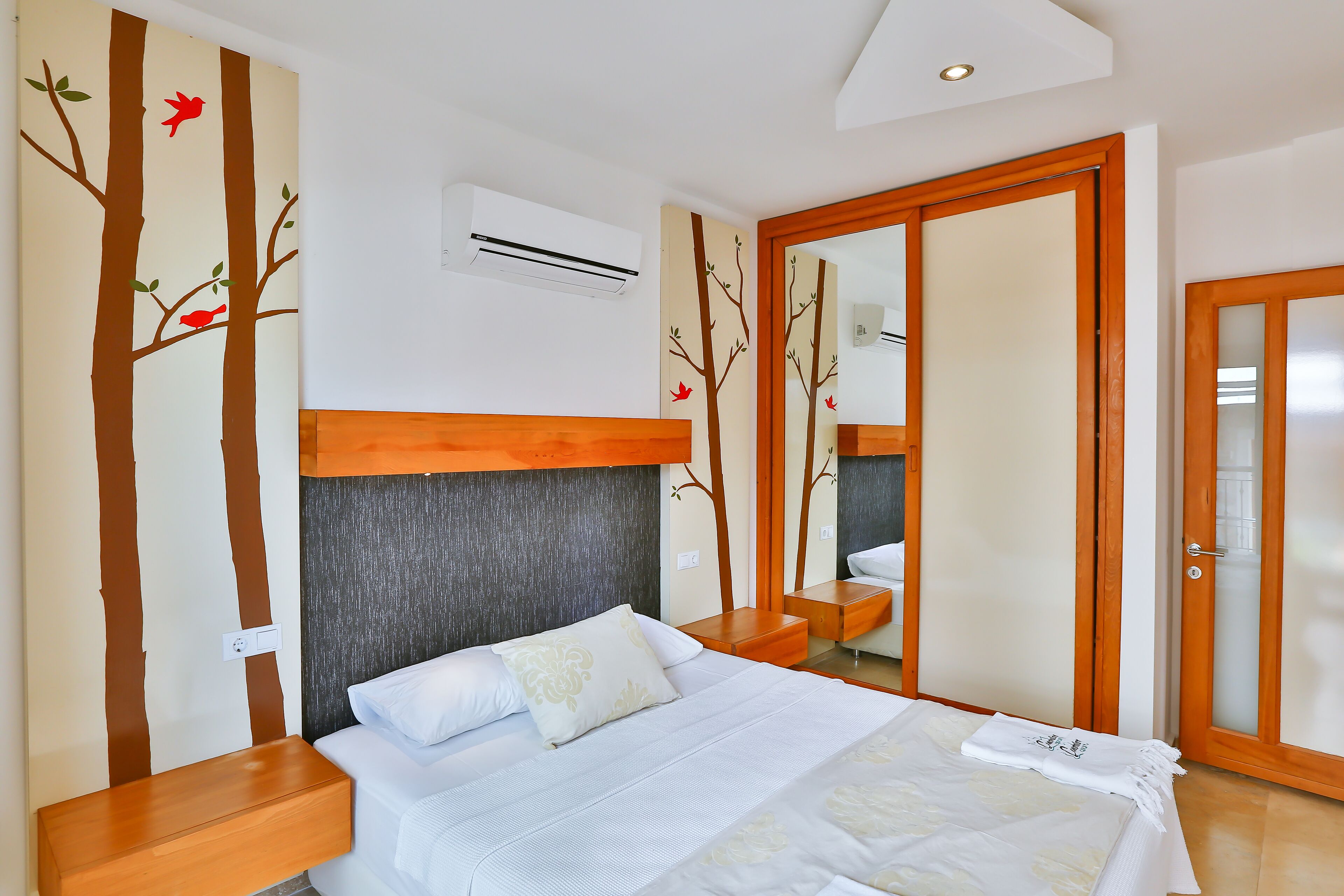 A bedroom with a bed, a wooden nightstand, a mirror, and a wardrobe with a sliding door.