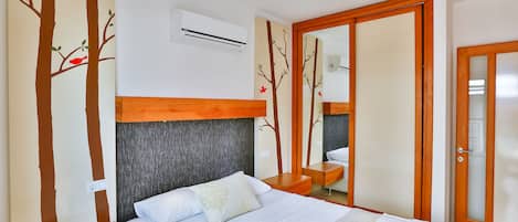 A bedroom with a bed, a wooden nightstand, a mirror, and a wardrobe with a sliding door.