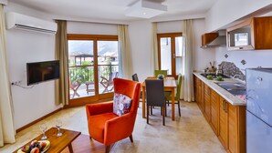 A modern kitchen with wooden cabinets, a built-in microwave, and a dining area with a table and chairs. - Cinarlar Apart Hotel (Kas)