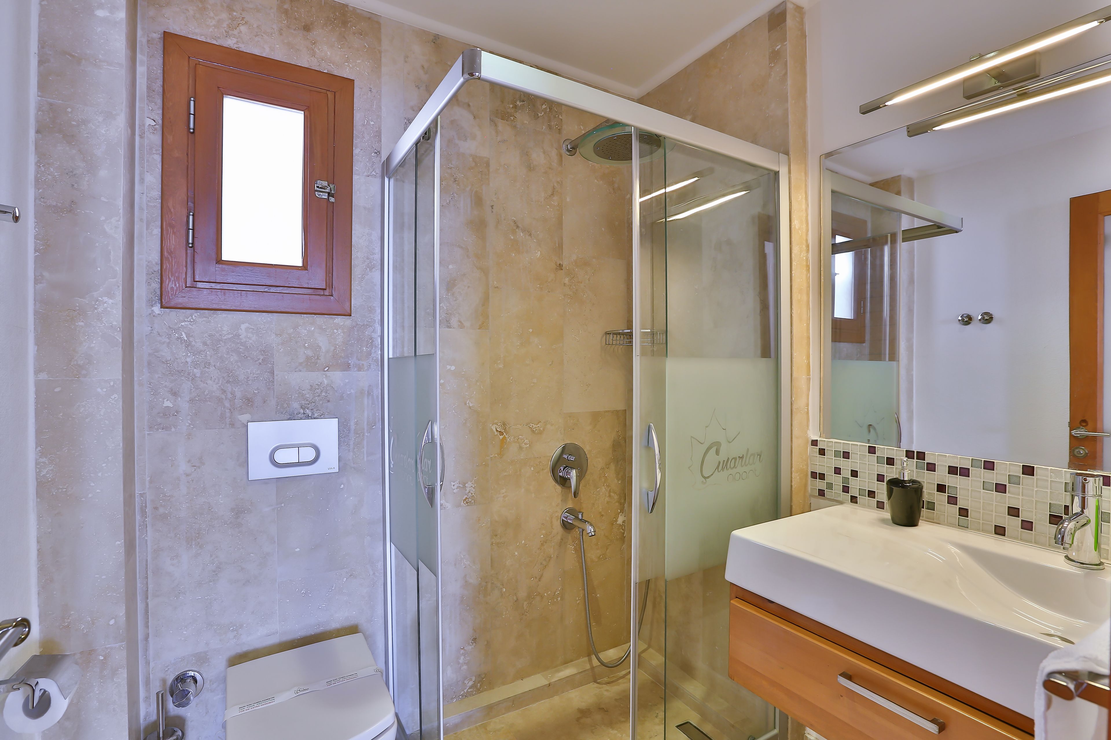 A modern bathroom with a glass-enclosed shower, a white sink, and a mirror with a decorative tile backsplash.