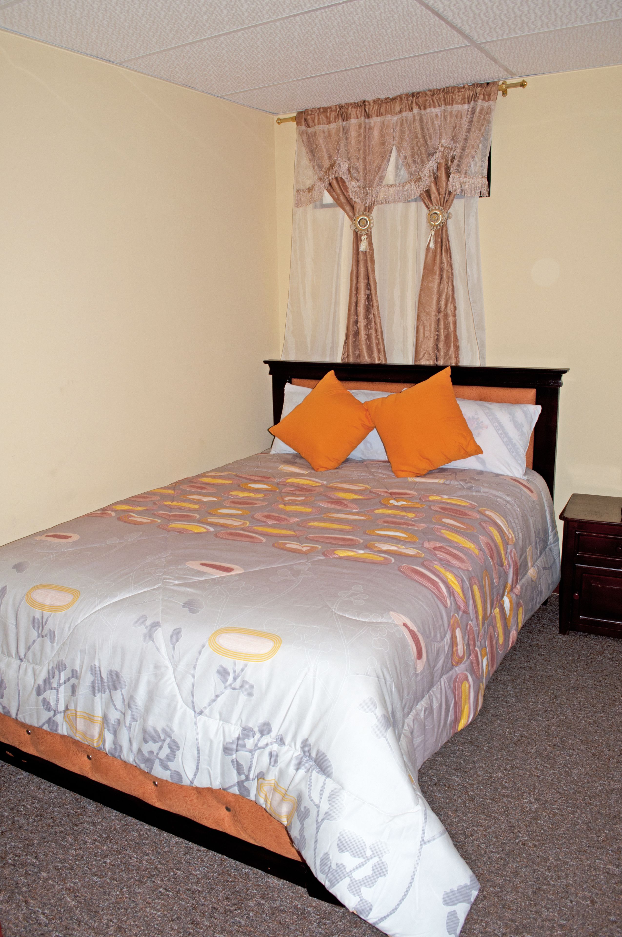 A neatly made bed with a patterned bedspread, two orange pillows, and a wooden headboard.