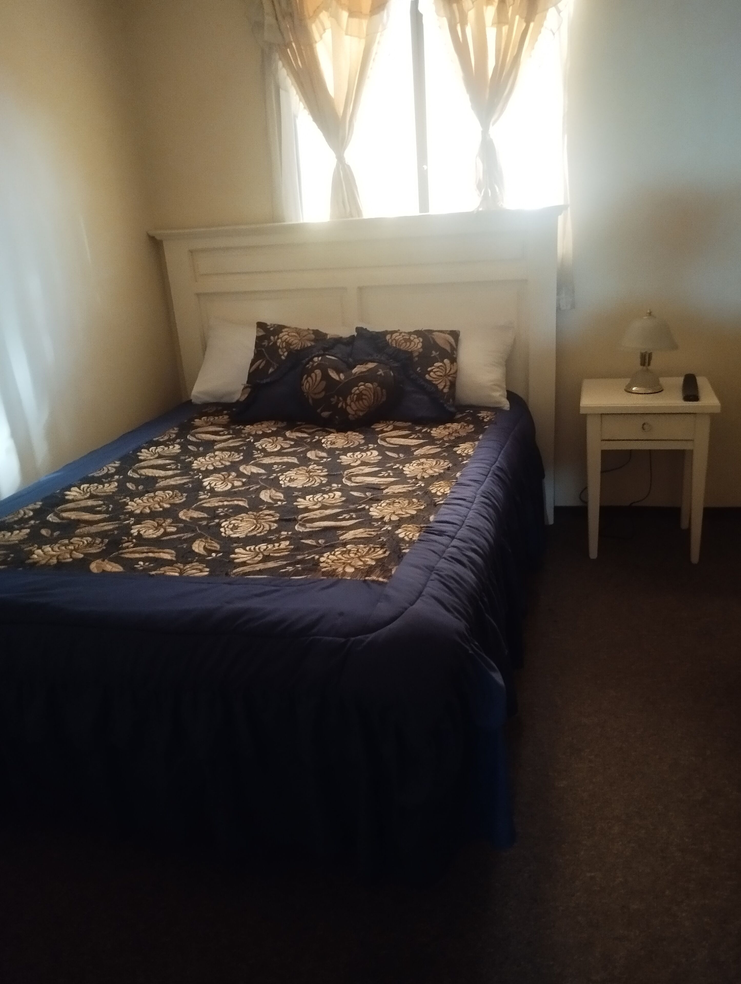 A bedroom with a bed, pillows, a nightstand, and a lamp.
