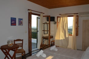 A bedroom with a bed, a chair, a small table, and a view of the landscape. - Vavoulas Village (Naxos)