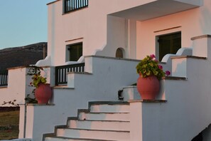 Ein weißes Gebäude mit einer Treppe, die zu einem Balkon führt, und Blumentöpfen auf dem Geländer, unter blauem Himmel.