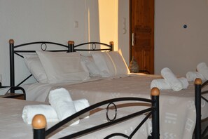 Ein Bett mit Metallgestell und Holzknöpfen, weiße Bettwäsche und eine Holztür im Hintergrund.