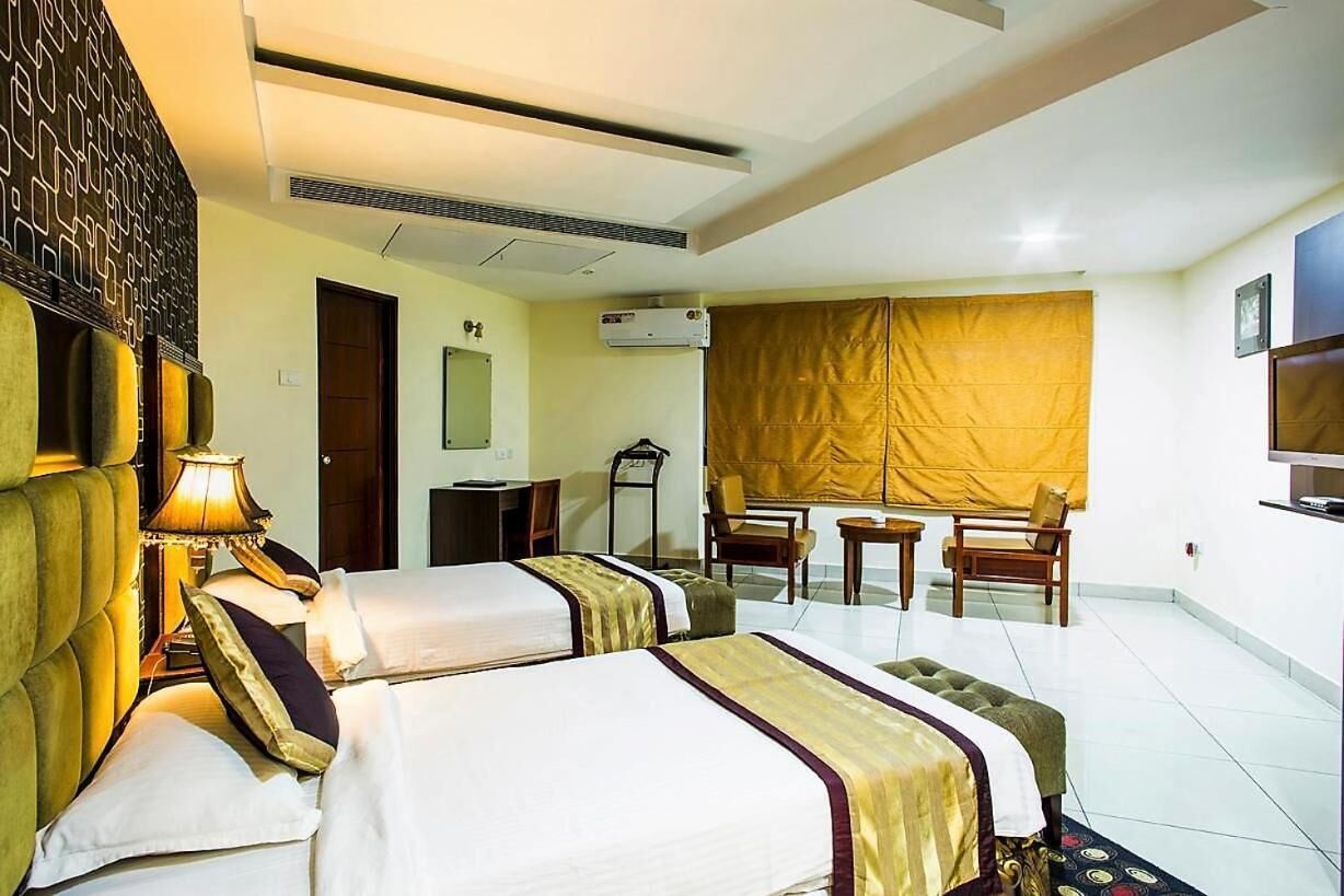 Habitación de hotel con dos camas, un escritorio, una silla, un equipo de aire acondicionado y un televisor.