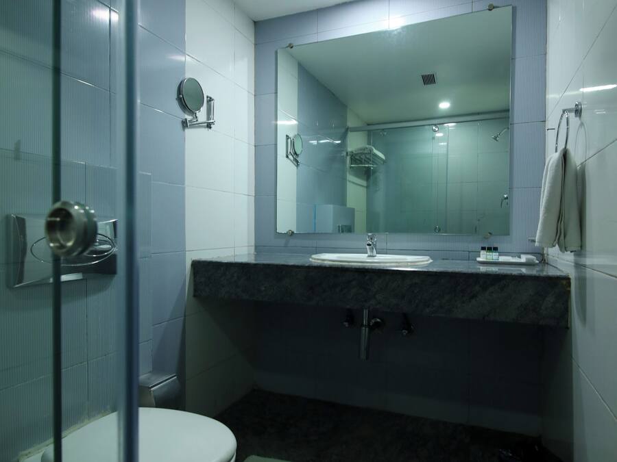 A modern bathroom with a glass shower enclosure, a white toilet, a marble sink, and a large mirror.