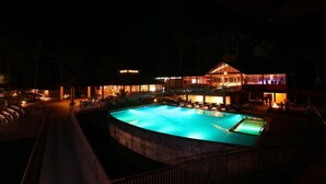 A nighttime view of a hotel with a swimming pool, outdoor seating, and a covered area with tables and chairs. - Kofiland Resort (Peermade)