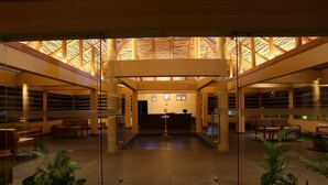 A spacious lobby with a high ceiling, glass partitions, and a central reception desk. - Kofiland Resort (Peermade)