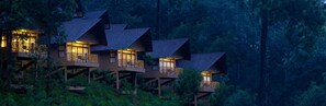 Une série de cabanes en bois surélevées, dotées de balcons, et entourées d’une forêt dense.