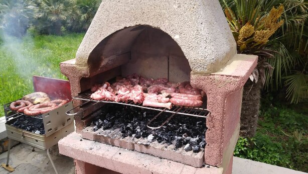 A concrete outdoor grill with a chimney, cooking sausages and chicken, and a charcoal grill with sausages. - Villa Elisa (Agerola)