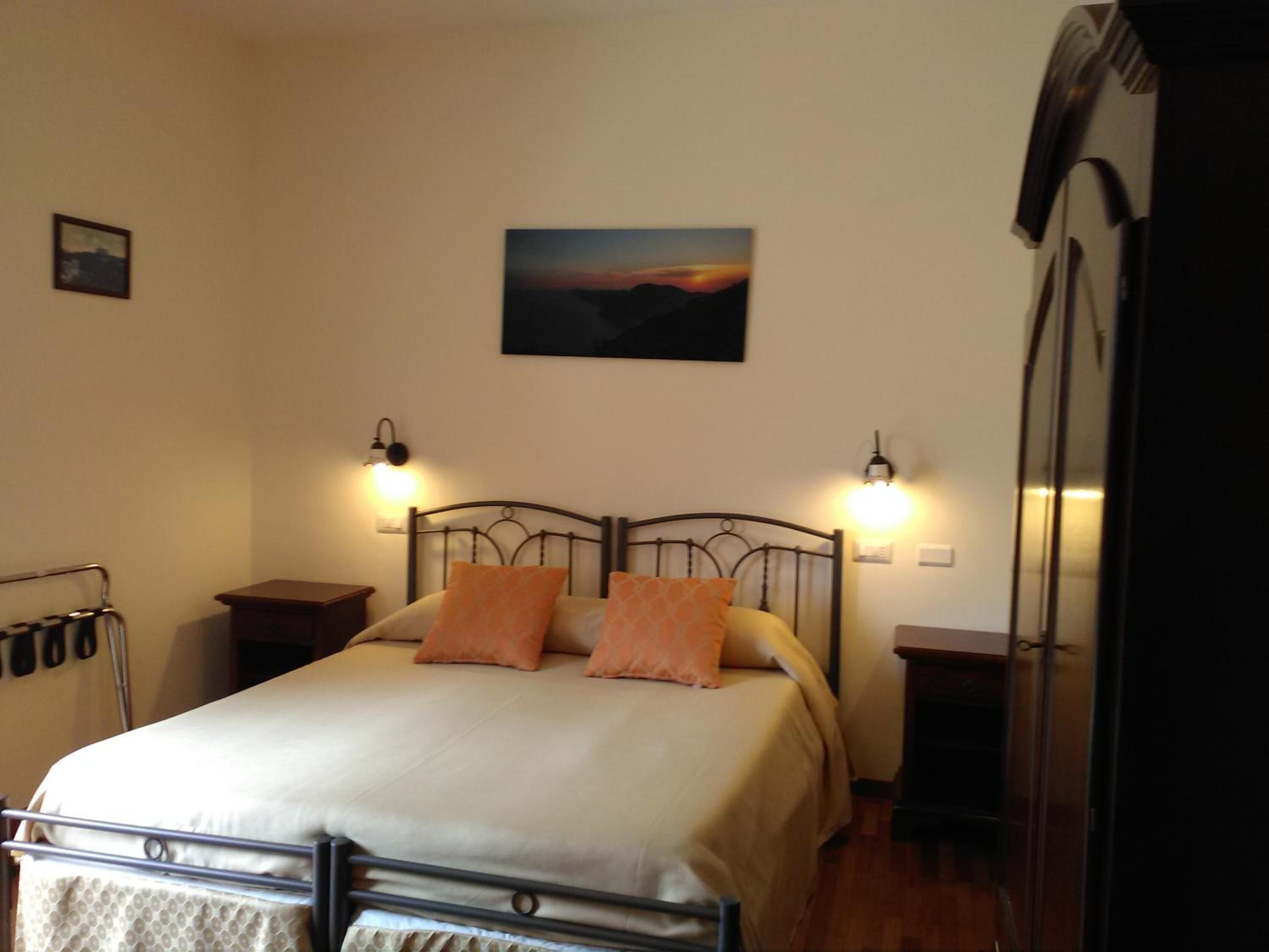 Un dormitorio con cama, dos mesitas de noche, un cuadro en la pared y un armario.