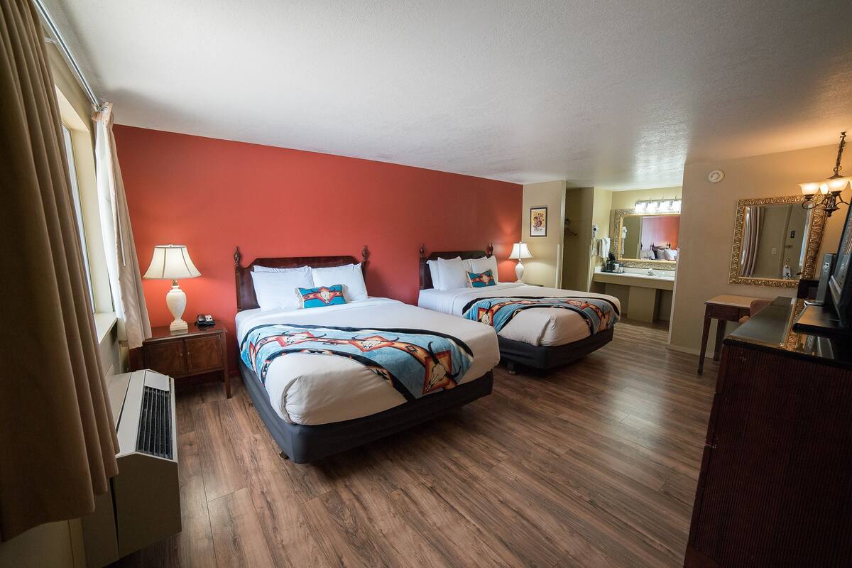 A hotel room with two beds, a mirror, a dresser, and a window with curtains.
