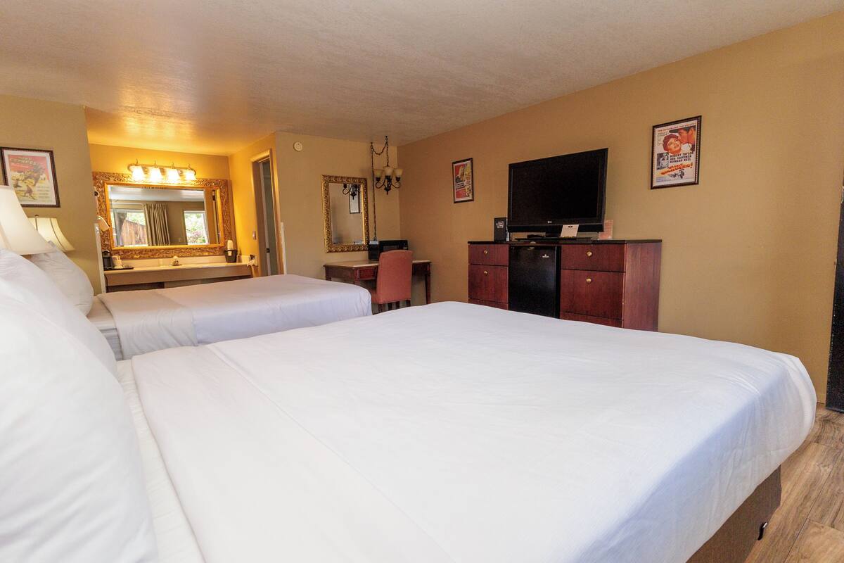 A hotel room with two beds, a desk, a chair, a TV, and a mirror.