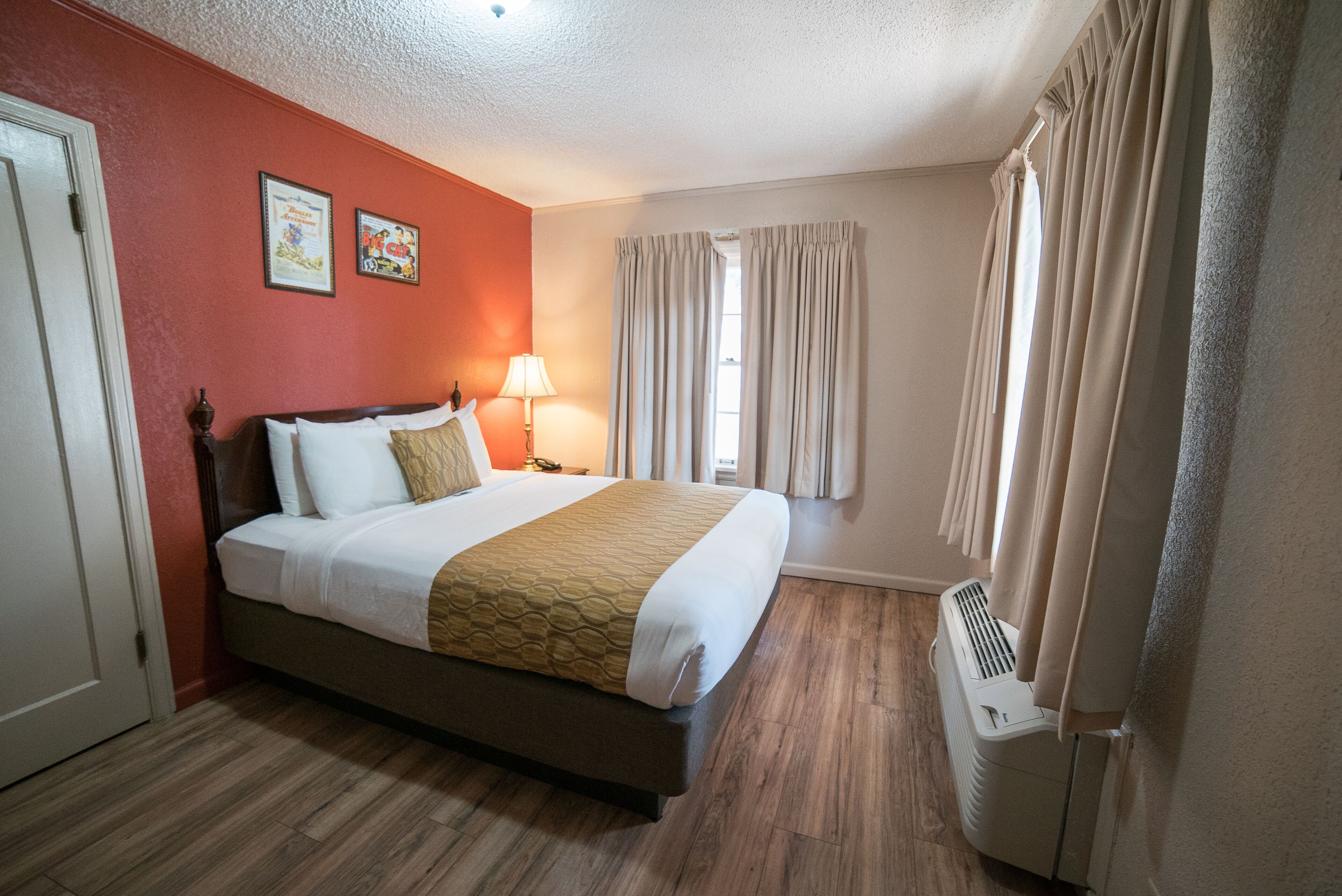 Hotellihuone, jossa on sänky, lamppu, verhot ja lämmitin.