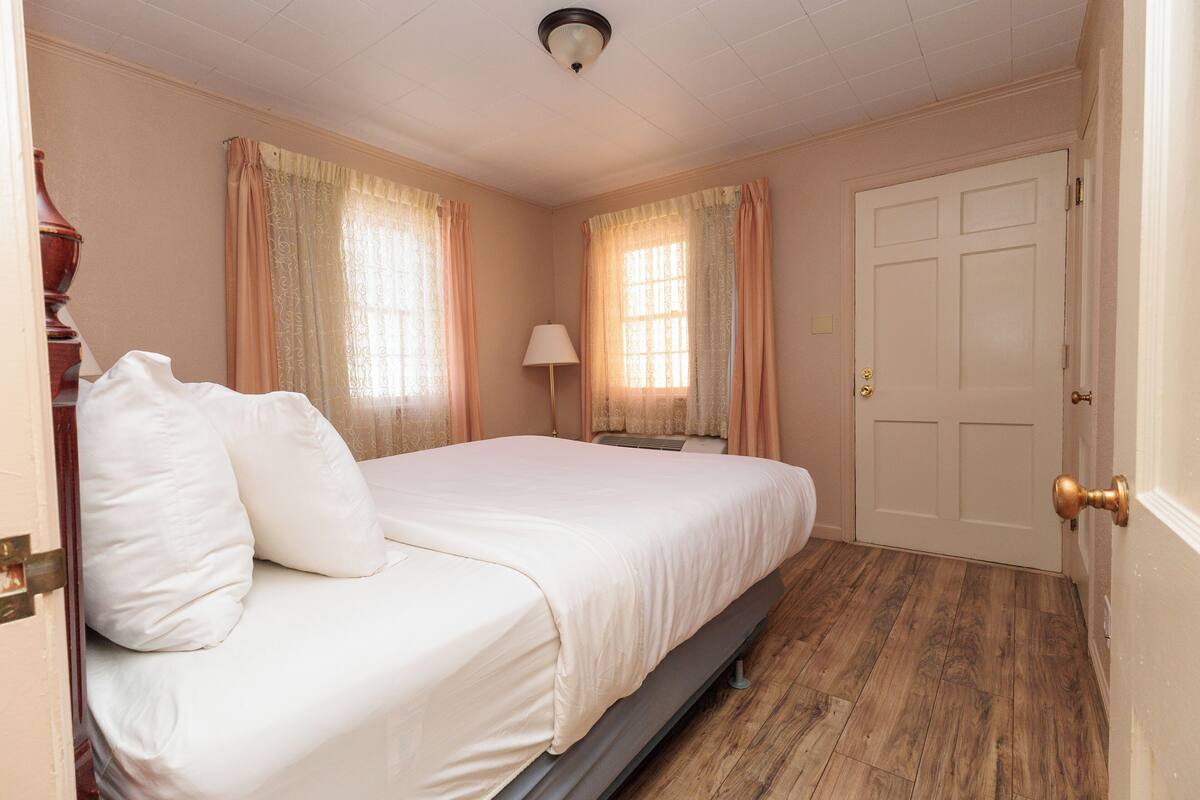 A bedroom with a bed, curtains, a lamp, and a door.
