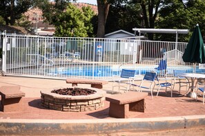 A swimming pool with a stone fire pit, surrounded by a white fence, and outdoor seating with a table and chairs. - Parry Lodge (Kanab)