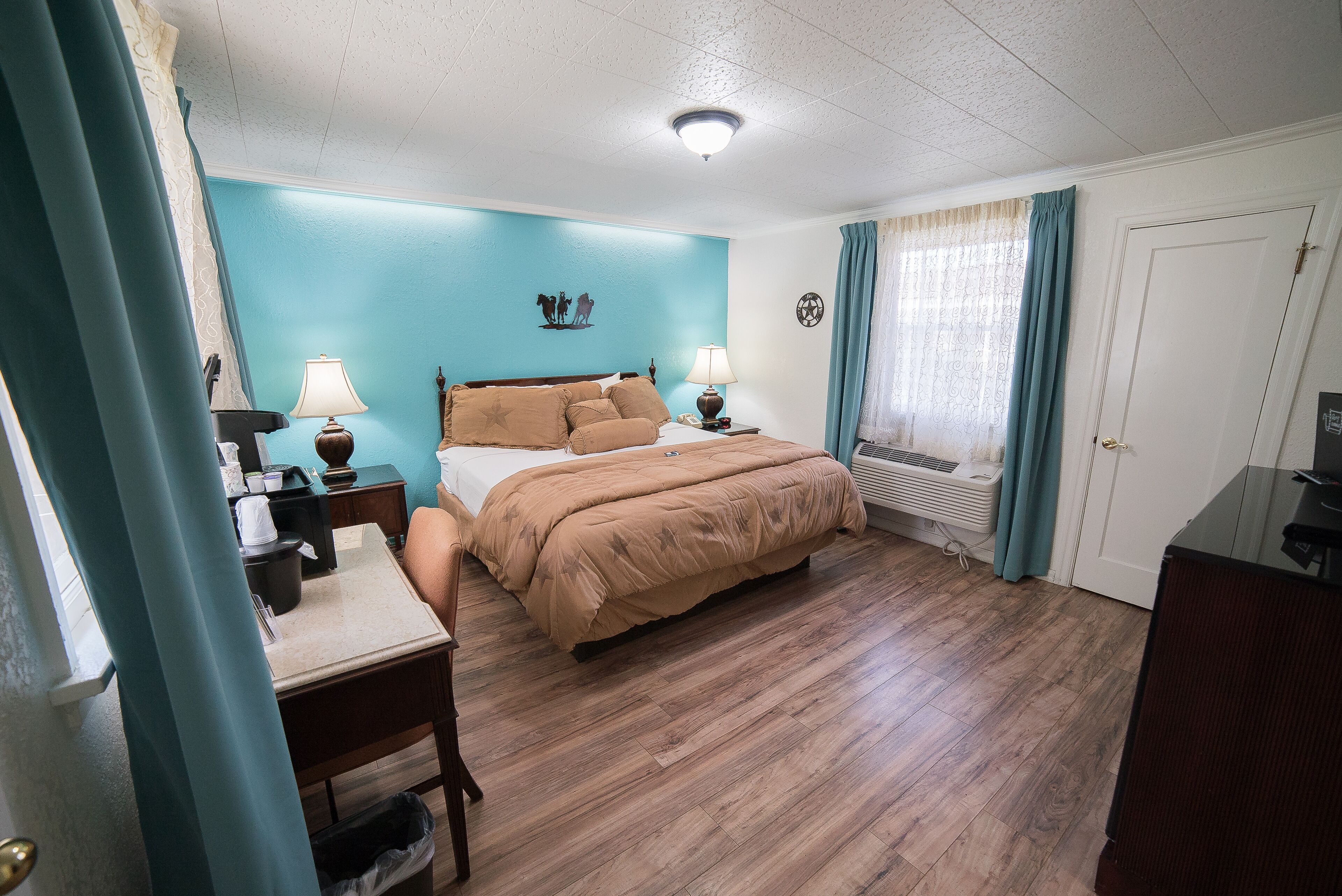 A bedroom with a bed, two bedside tables with lamps, a dresser, a desk, and a window with curtains.