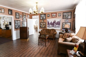 A cozy living room with a brown leather sofa, a glass coffee table, and a wooden cabinet. The room features a wooden floor, a chandelier, and walls adorned with framed photographs. - Parry Lodge (Kanab)